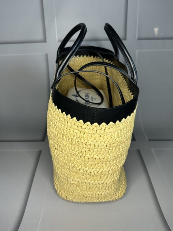 A yellow crocheted bag with black handles.