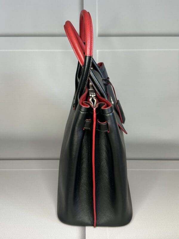 A black purse with red handles and a zipper.