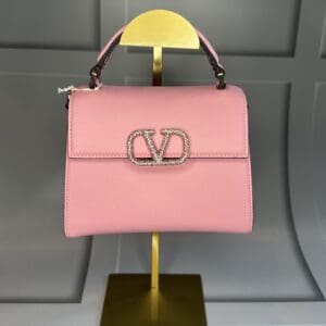 A pink bag is on display in front of a wall.